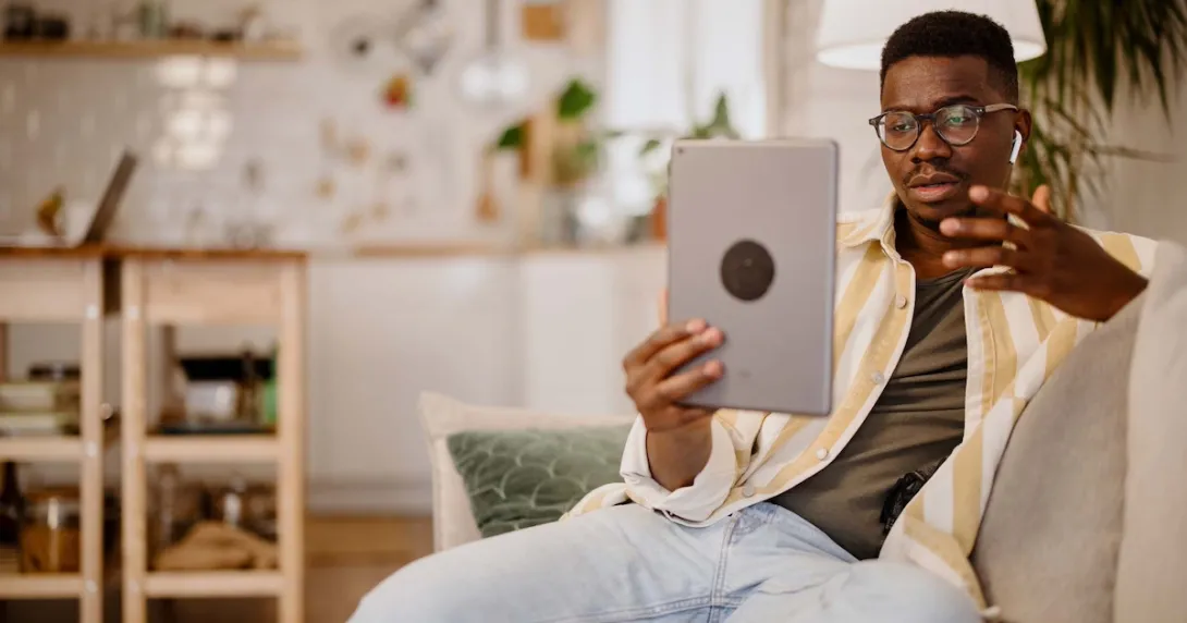 Person sitting on the couch in a home while holding up a tablet in front of them
