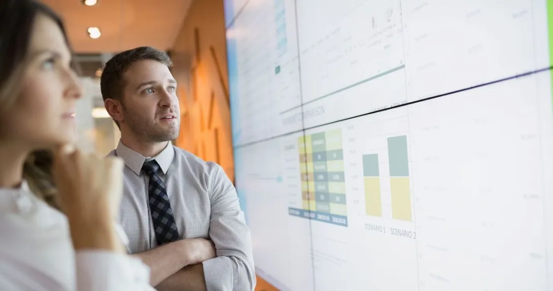 Two businesspeople looking at charts displayed on a large screen