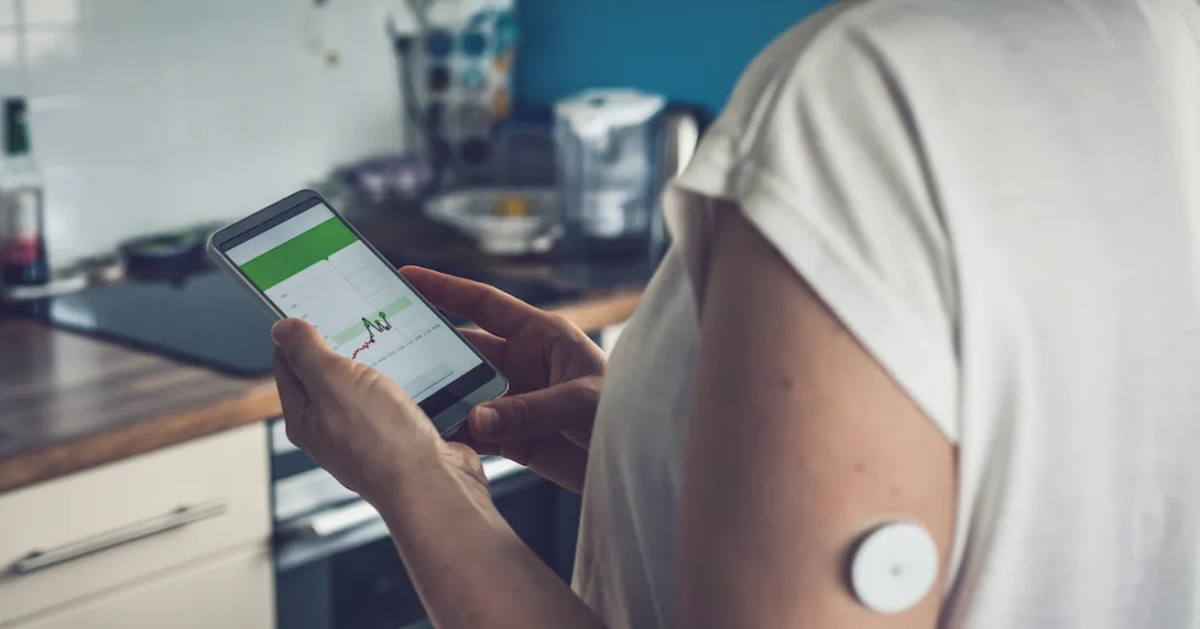 Woman checking glucose level with a remote sensor and mobile phone.