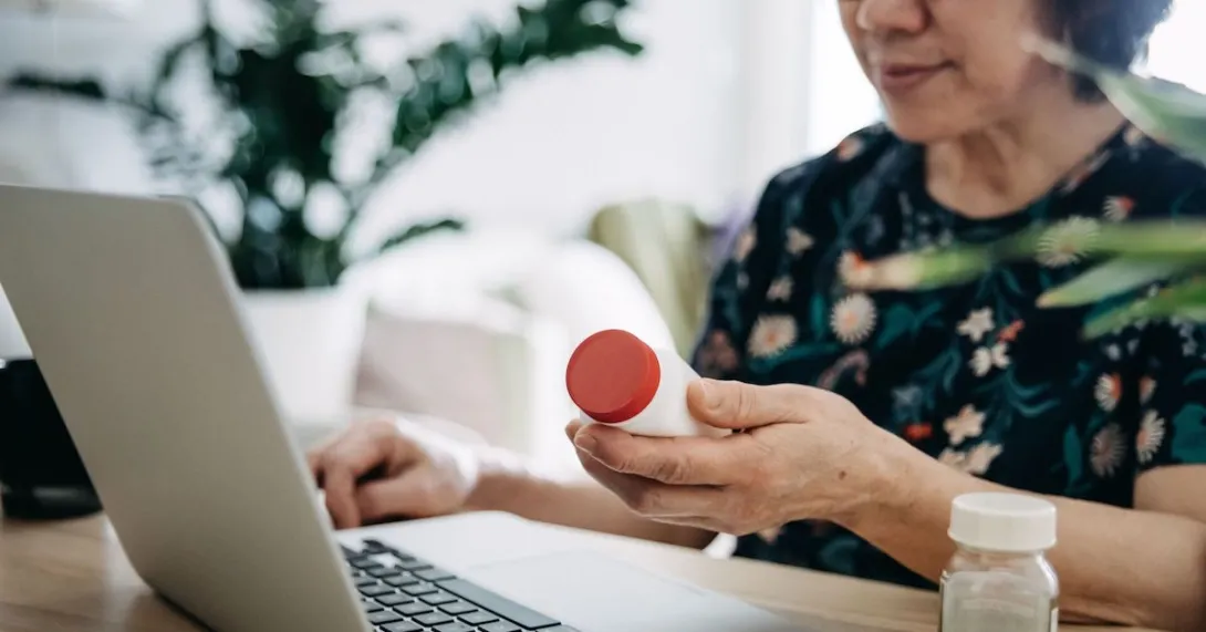 A person holding a pill bottle while using a laptop.