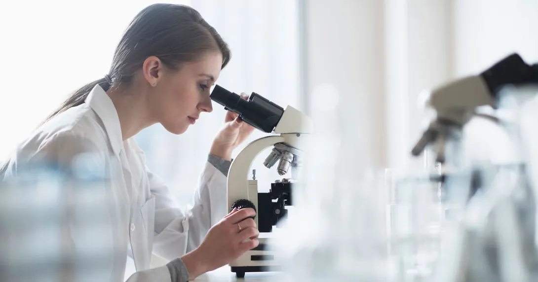 A lab technician analyzing a sample through a microscope