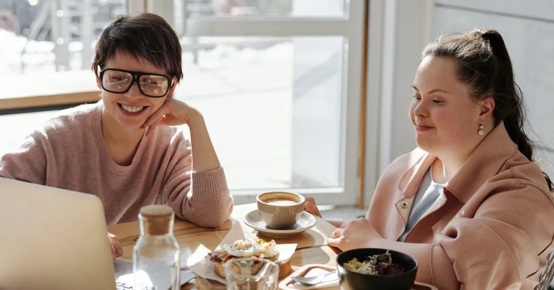 A person with Down syndrome with a friend watching from a laptop