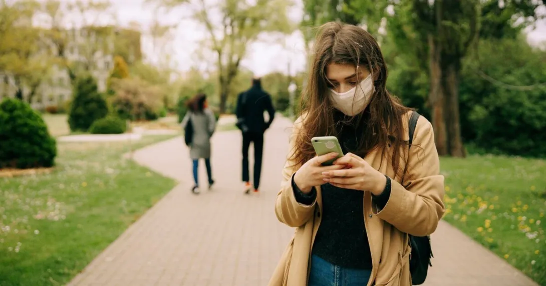 A person wearing mask is typing on their phone