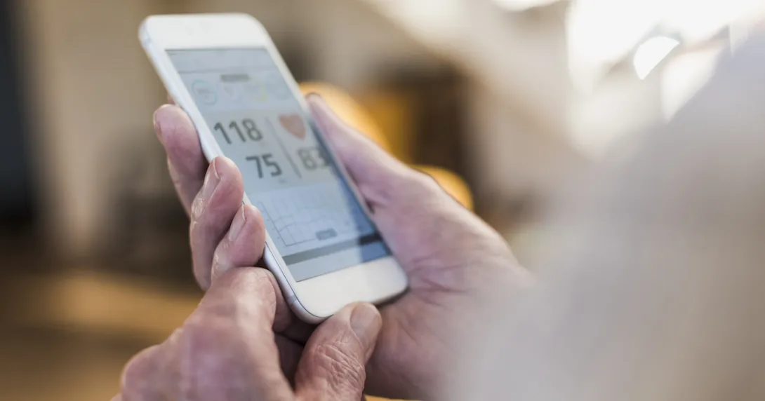 A close-up of a person holding a smartphone displaying heart rate and blood pressure data