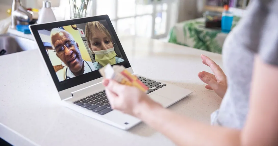 A close up of a woman holding a bottle of pills while talking to two providers via telehealth