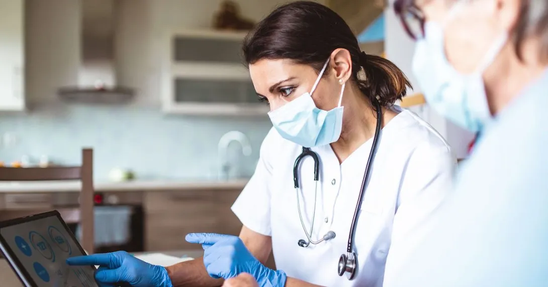 Healthcare providers in lab coats wearing a mask and stethoscope and looking at a screen