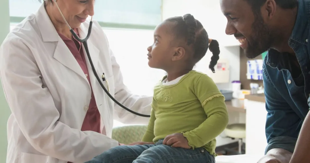Healthcare provider and another adult standing by a child on an exam table