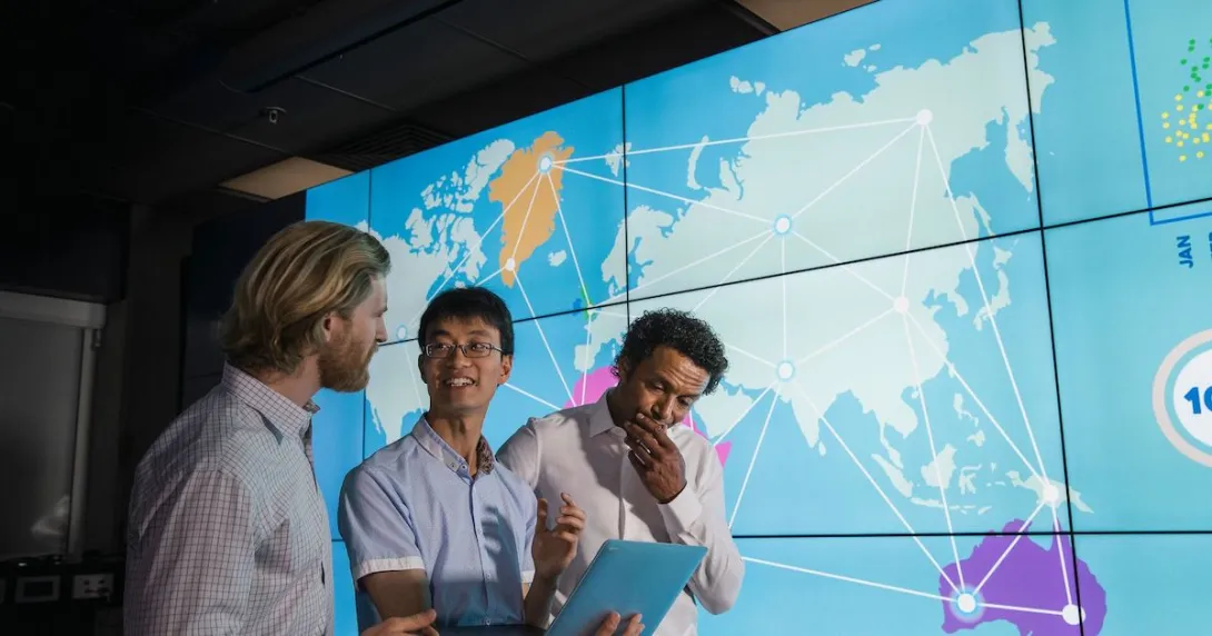 Three people standing in front of a large board showing the world map