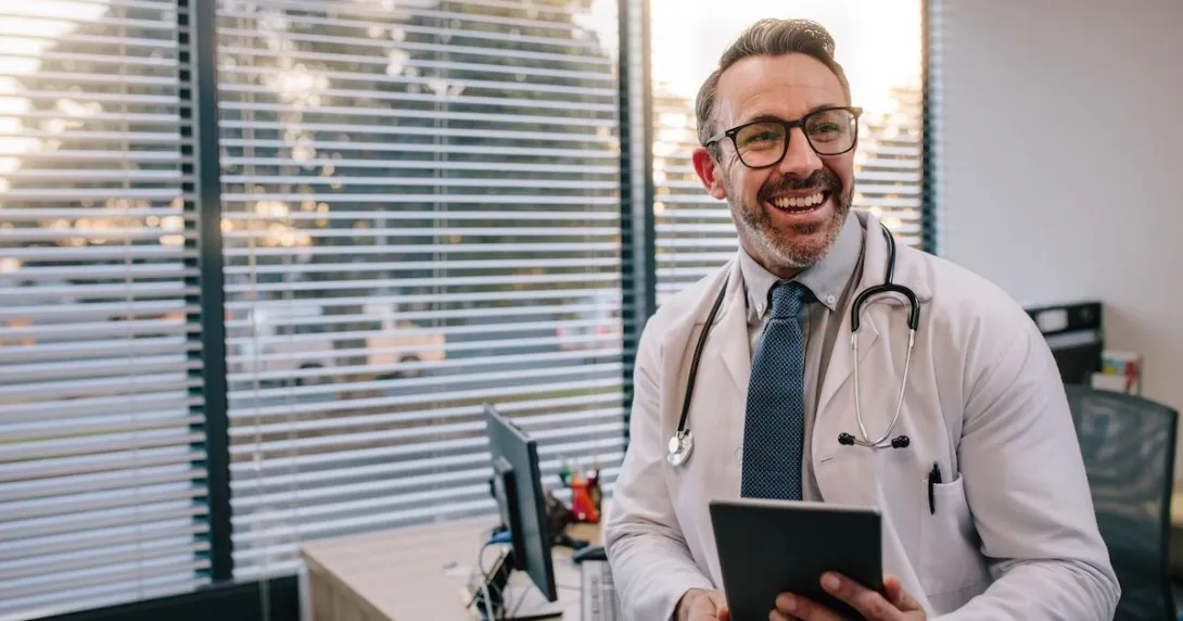 Healthcare provider wearing a lab coat and stethoscope holding a tablet