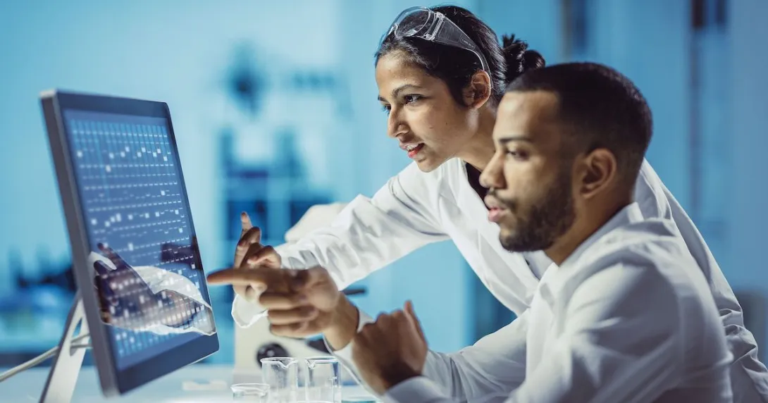 Two individuals, one sitting down and the other standing up, looking at a computer together