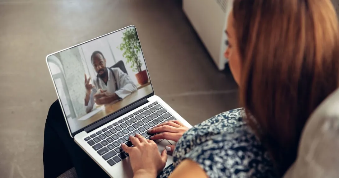 Person sitting on their couch with a computer on their lap talking to a virtual healthcare provider