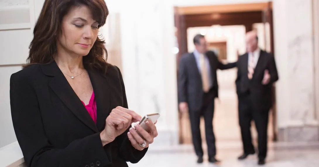 One person looking at their phone with two people blurred in the background