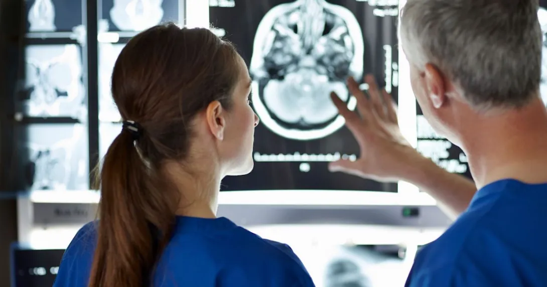 Two healthcare providers looking at a diagnostic image of a brain on a wall