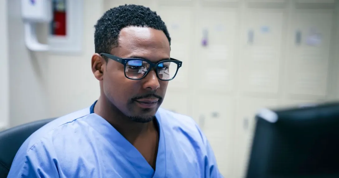 Healthcare provider wearing glasses, sitting in front of a computer monitor